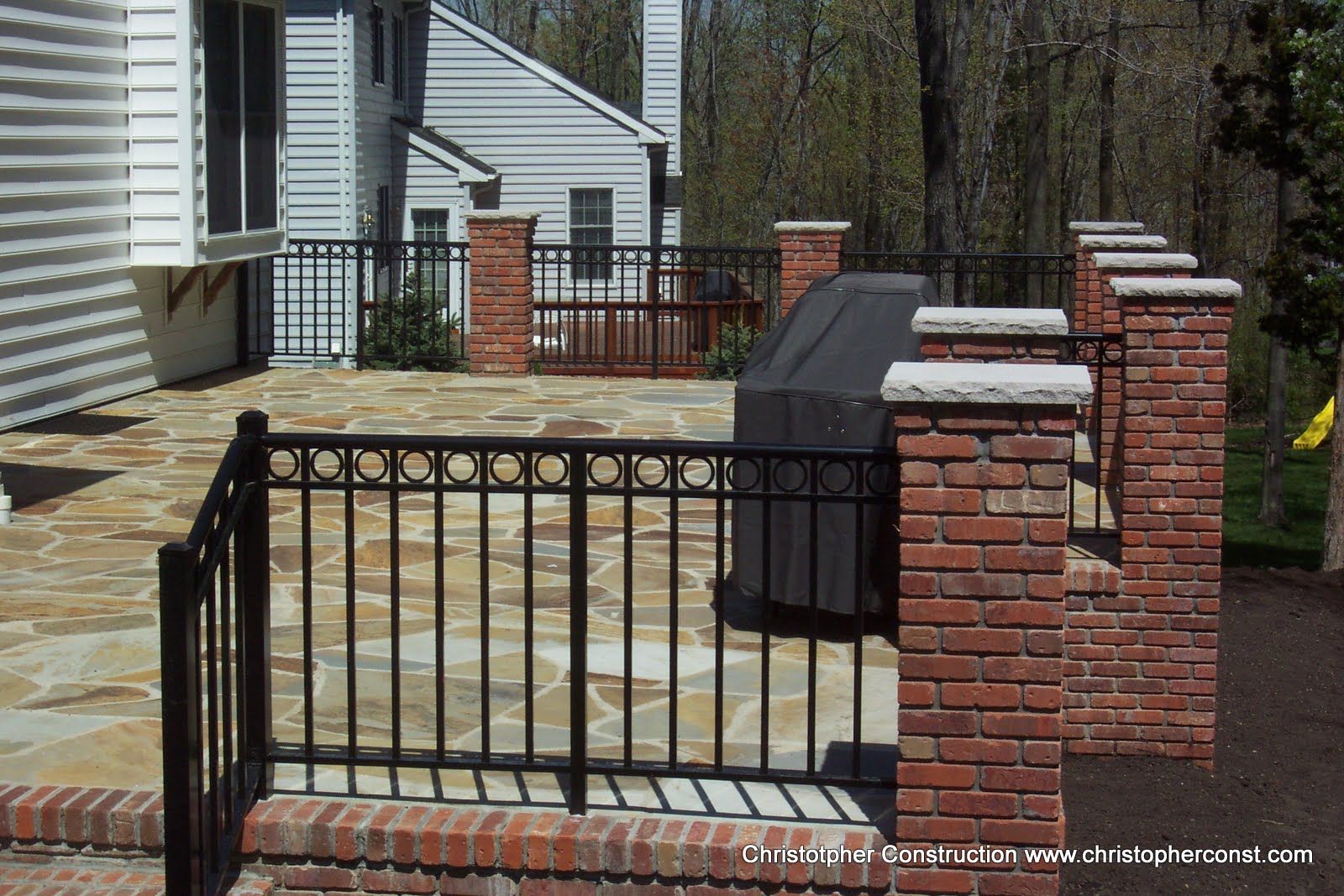 Black metal gate and brick pillars around a patio with a grill beside a house