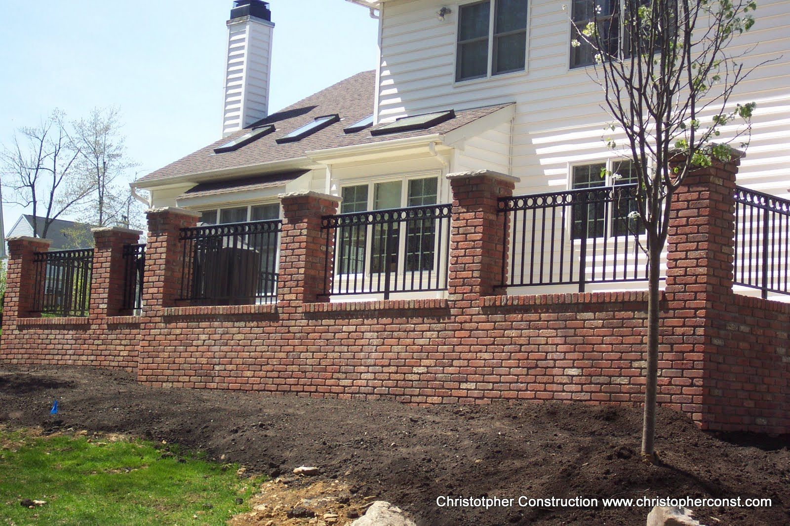 Brick house with a fenced patio and stone retaining wall in a sunny yard
