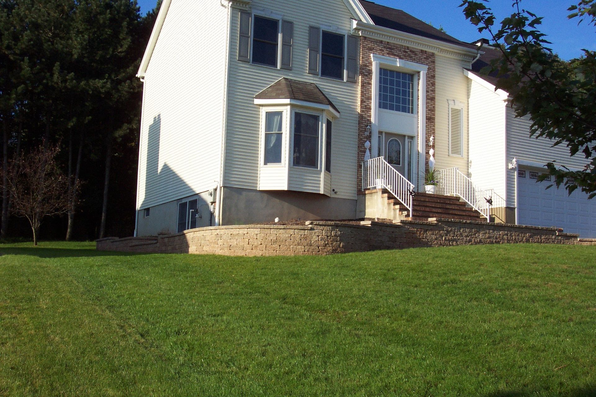 White two-story house with a bay window and front steps, set on a grassy lawn in daylight