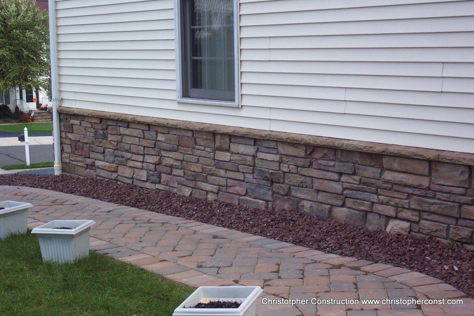 House exterior with stone veneer, white siding, and a paved walkway beside a lawn