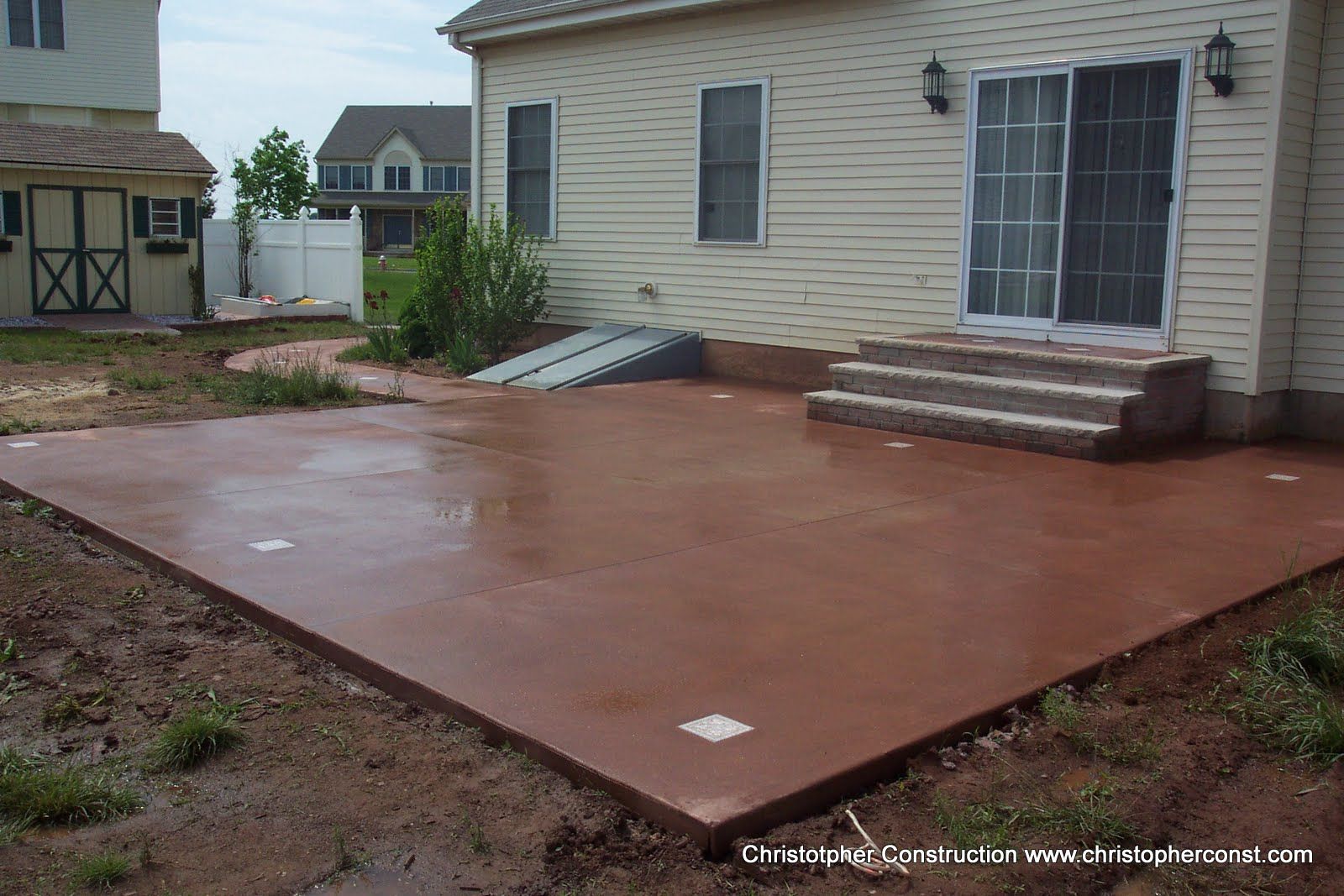Large red concrete patio beside a beige house with steps and siding back door