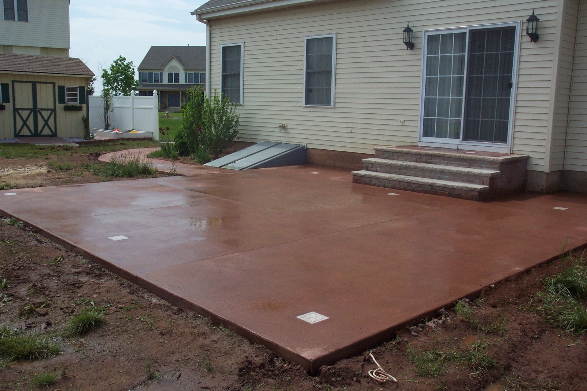 Fresh concrete patio slab beside a beige house in a backyard under construction