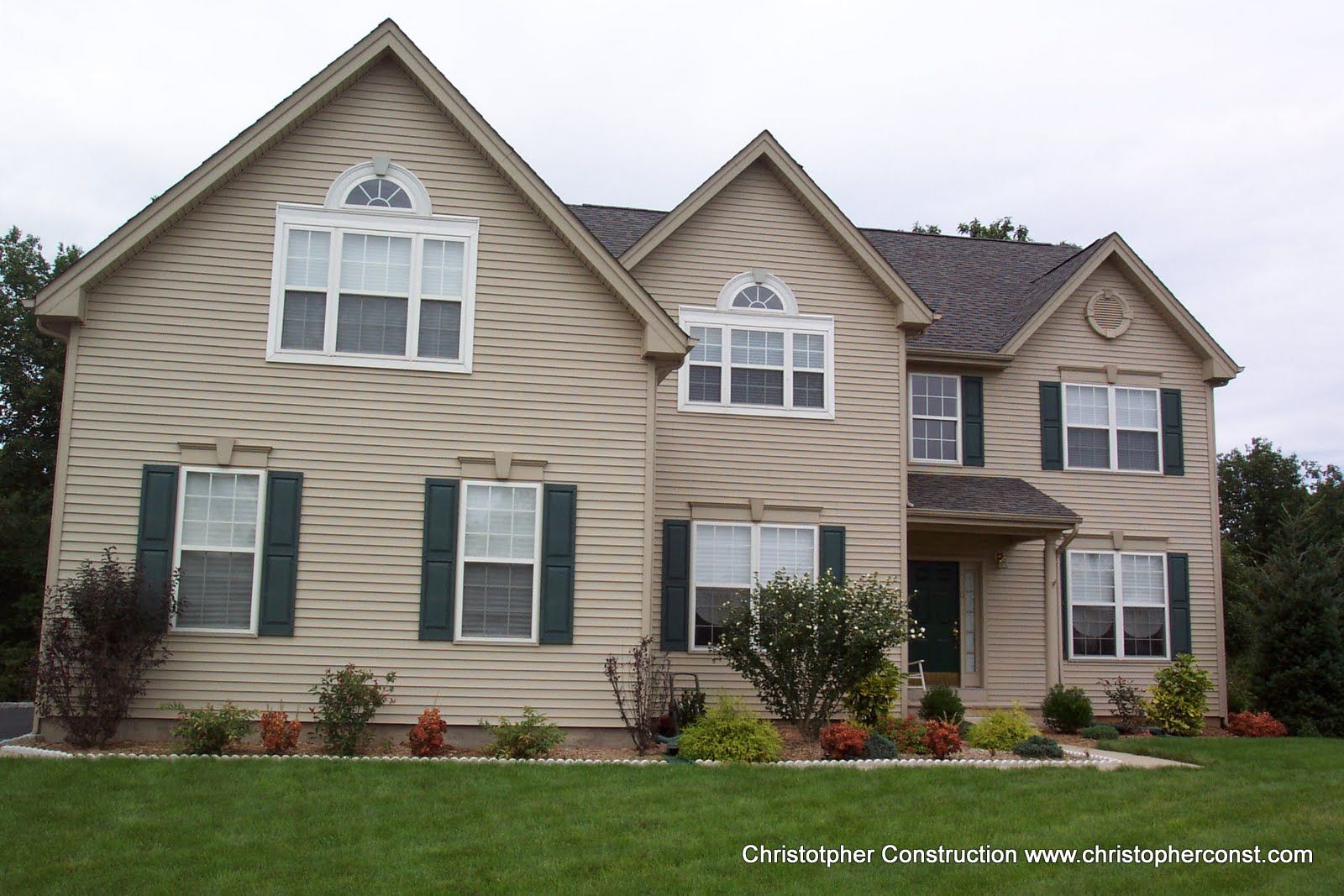 Suburban beige two-story house with green shutters, front porch, and landscaped yard