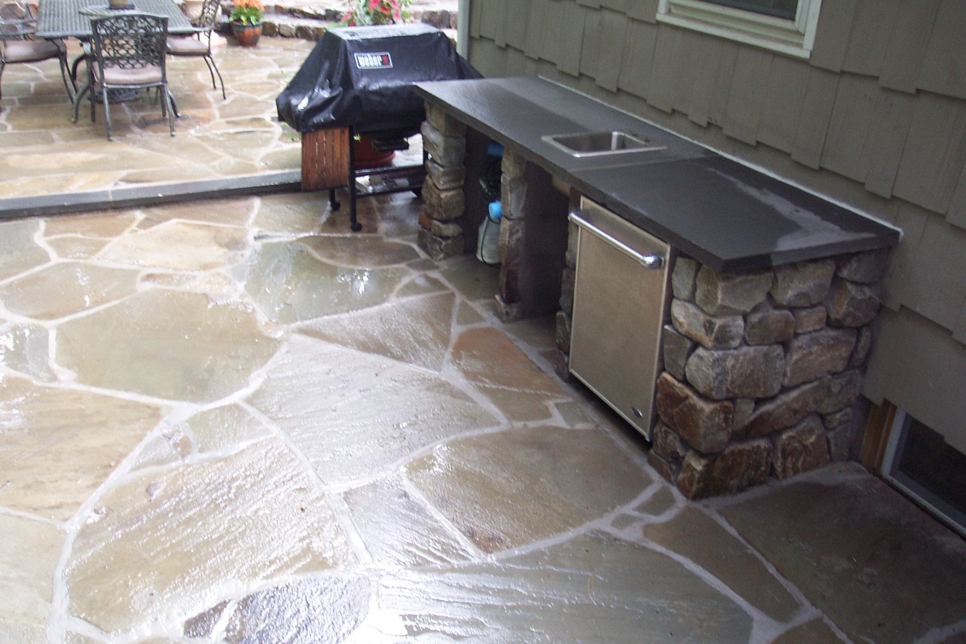 Stone patio with a built-in outdoor grill and counter, wet from recent cleaning or rain.