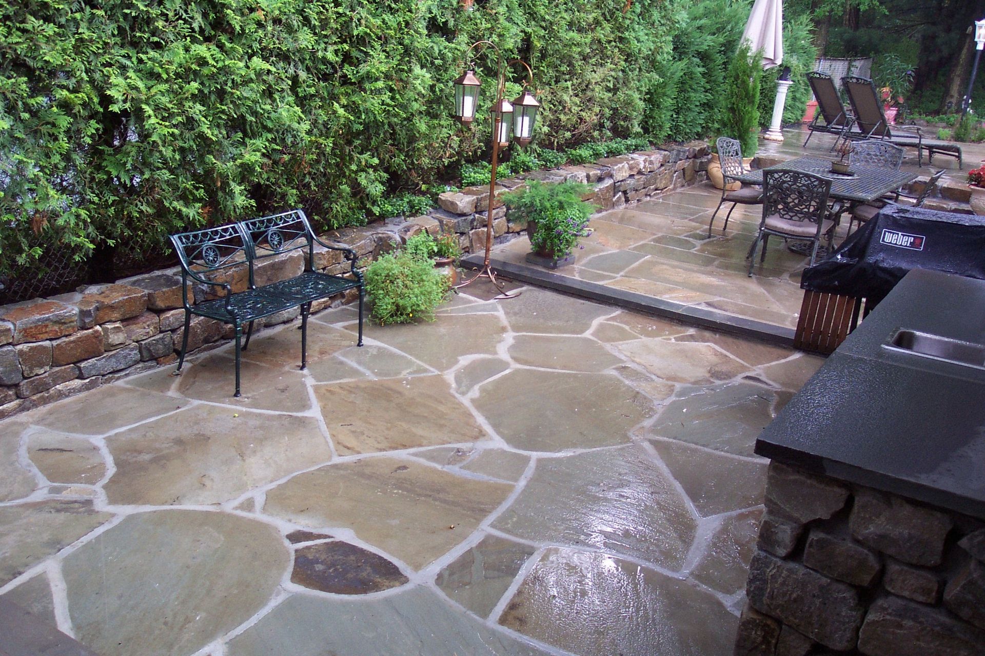 Stone patio with benches, potted plants, and a small water feature beside a garden wall