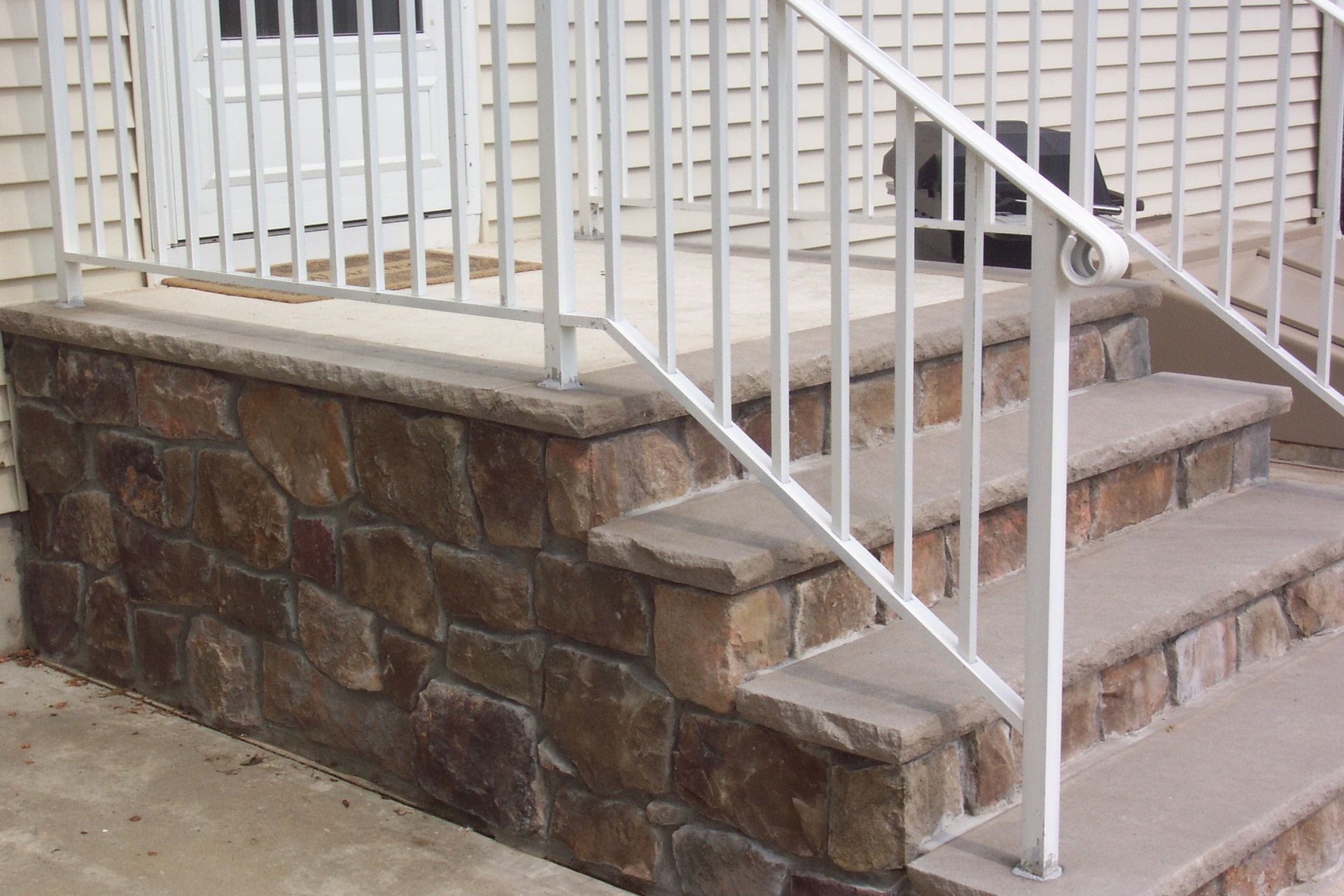 Stone porch steps with a white metal railing beside a house exterior