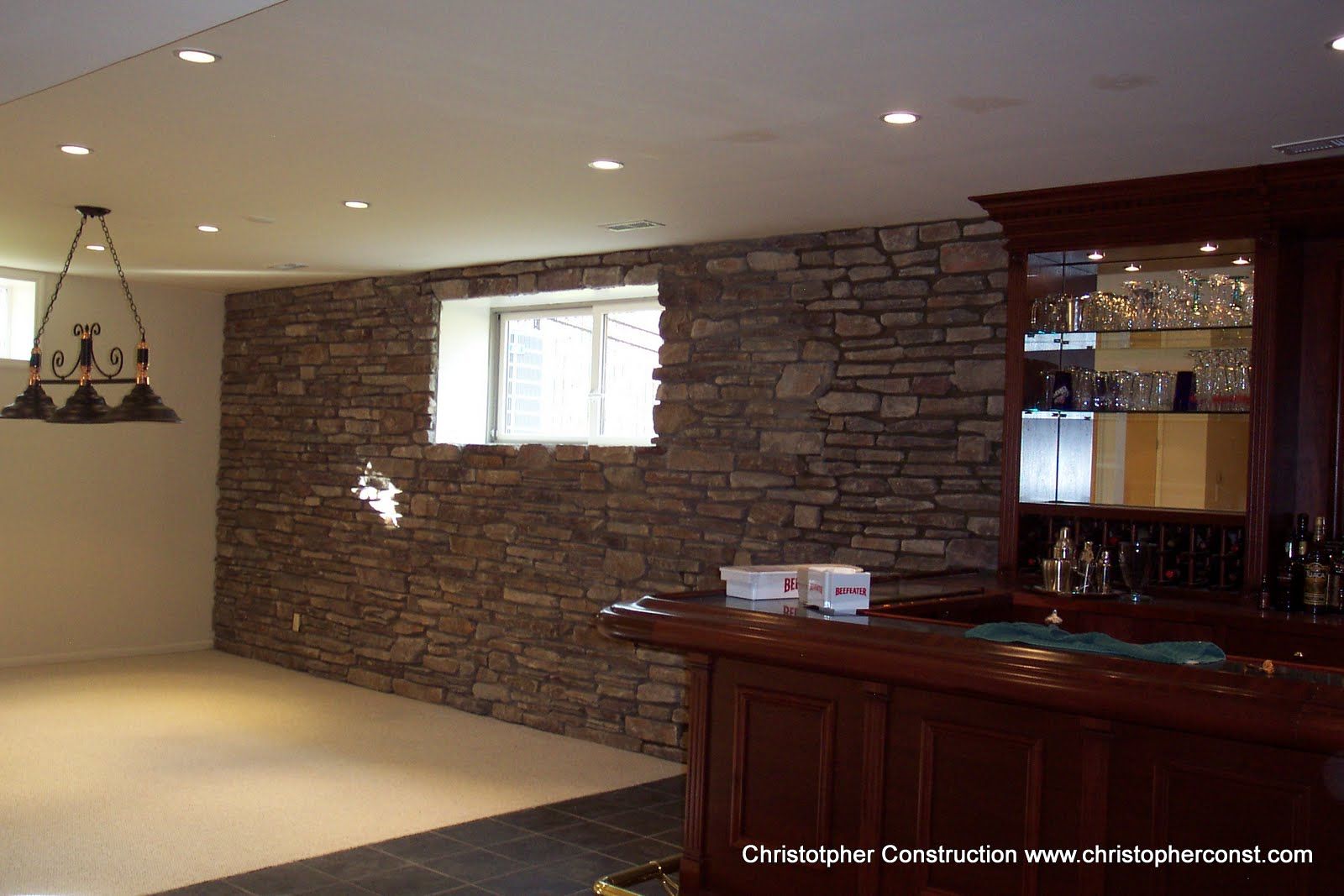 Basement with stone accent wall, recessed lights, and a dark wood wet bar with glass cabinets