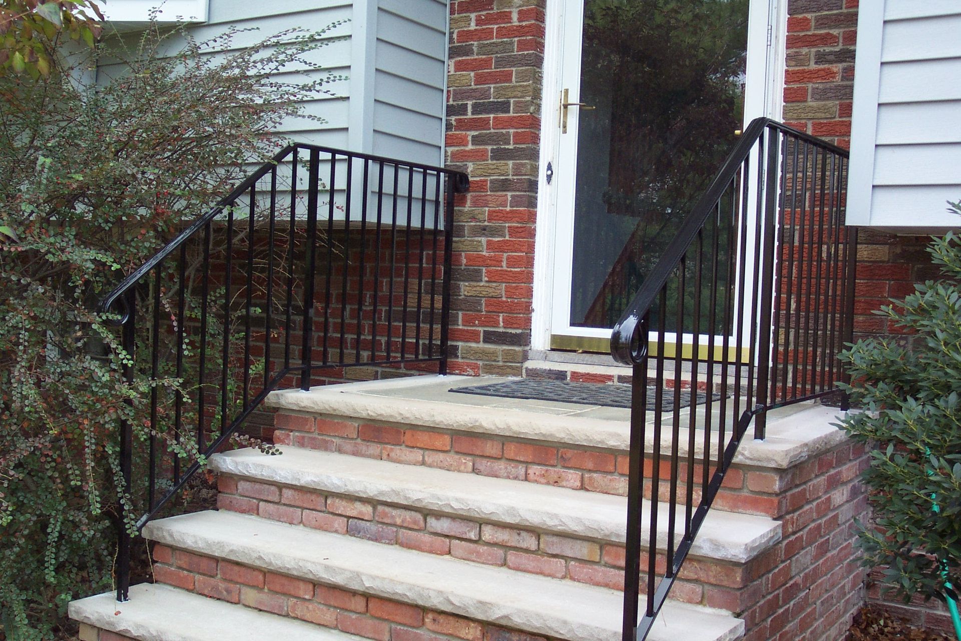 Brick front steps with black railings leading to a white front door.