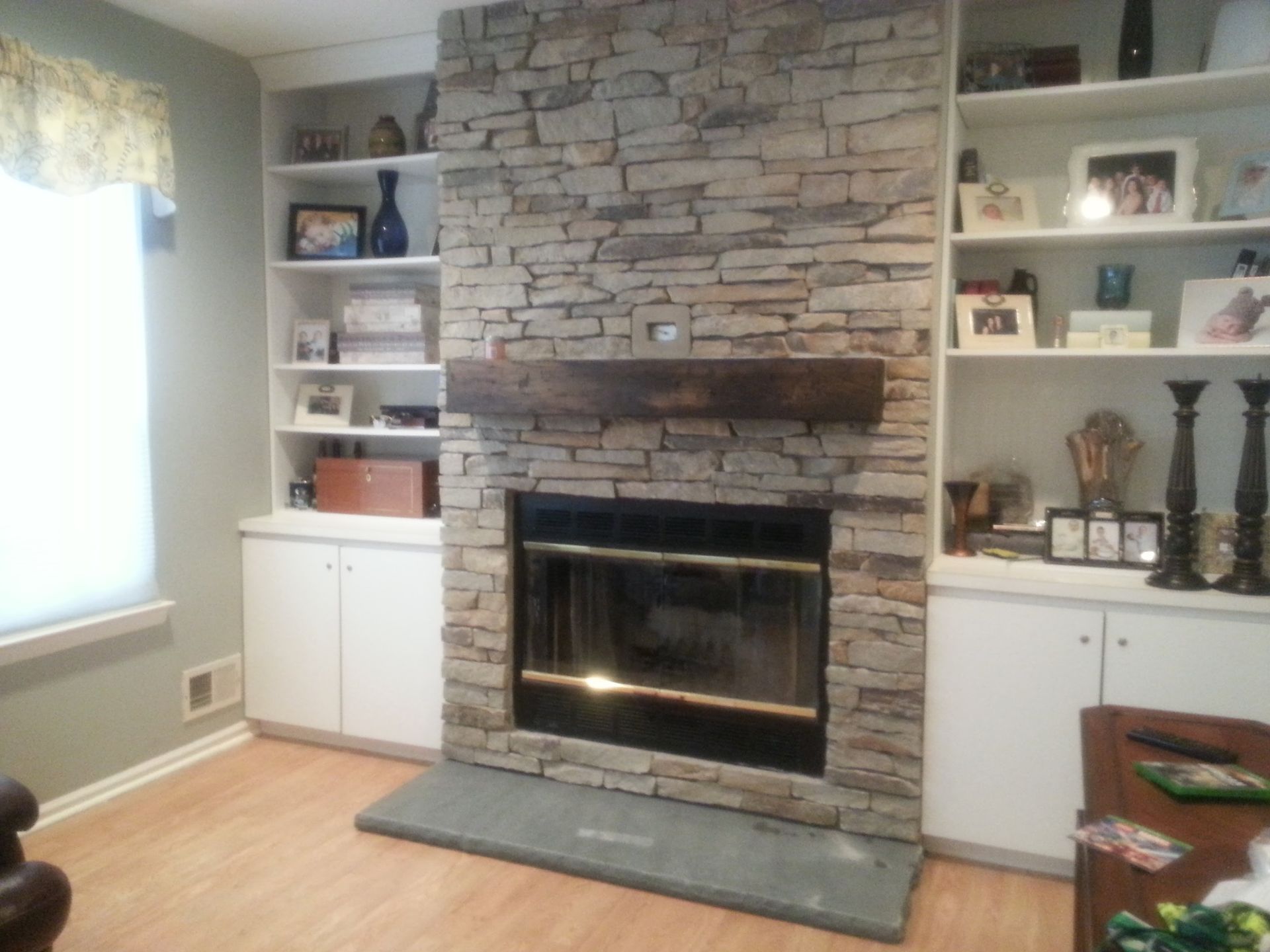 Living room fireplace with stone surround, built-in white shelves, and a window seat on the left