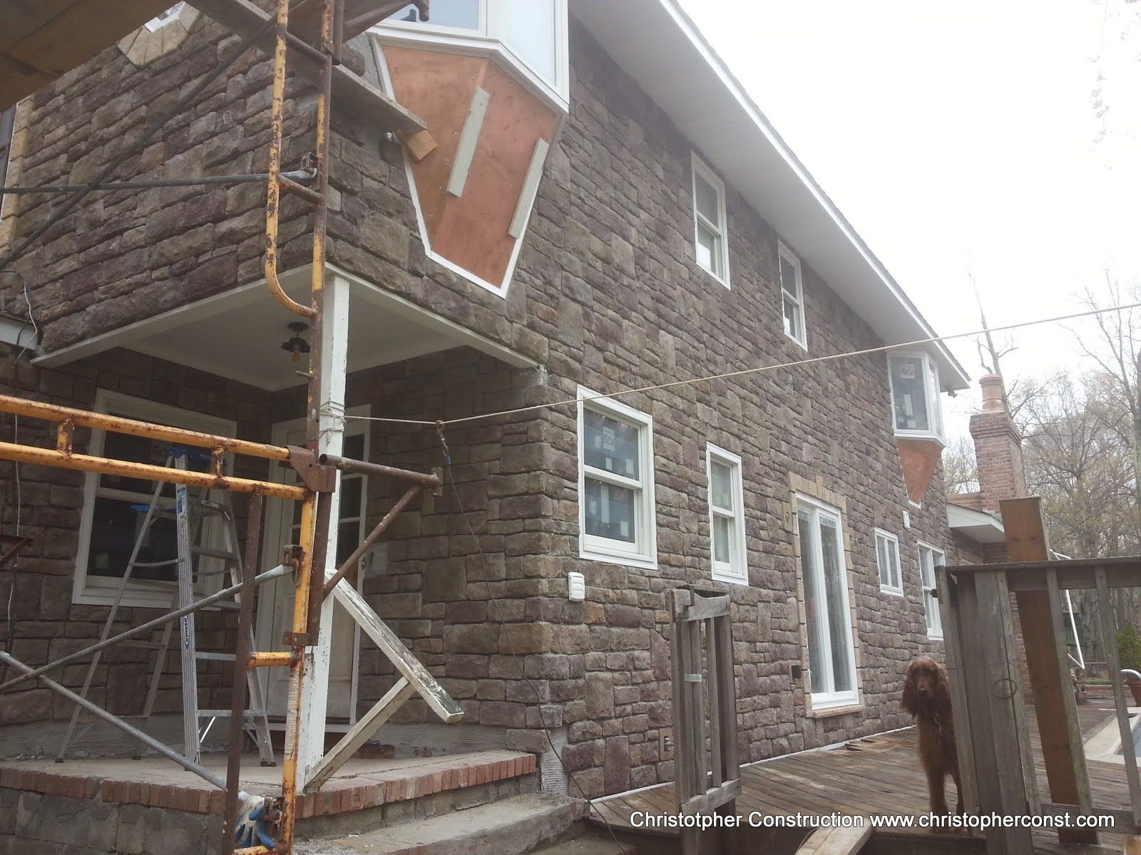 Stone house exterior with scaffolding and a small porch, viewed from the side.