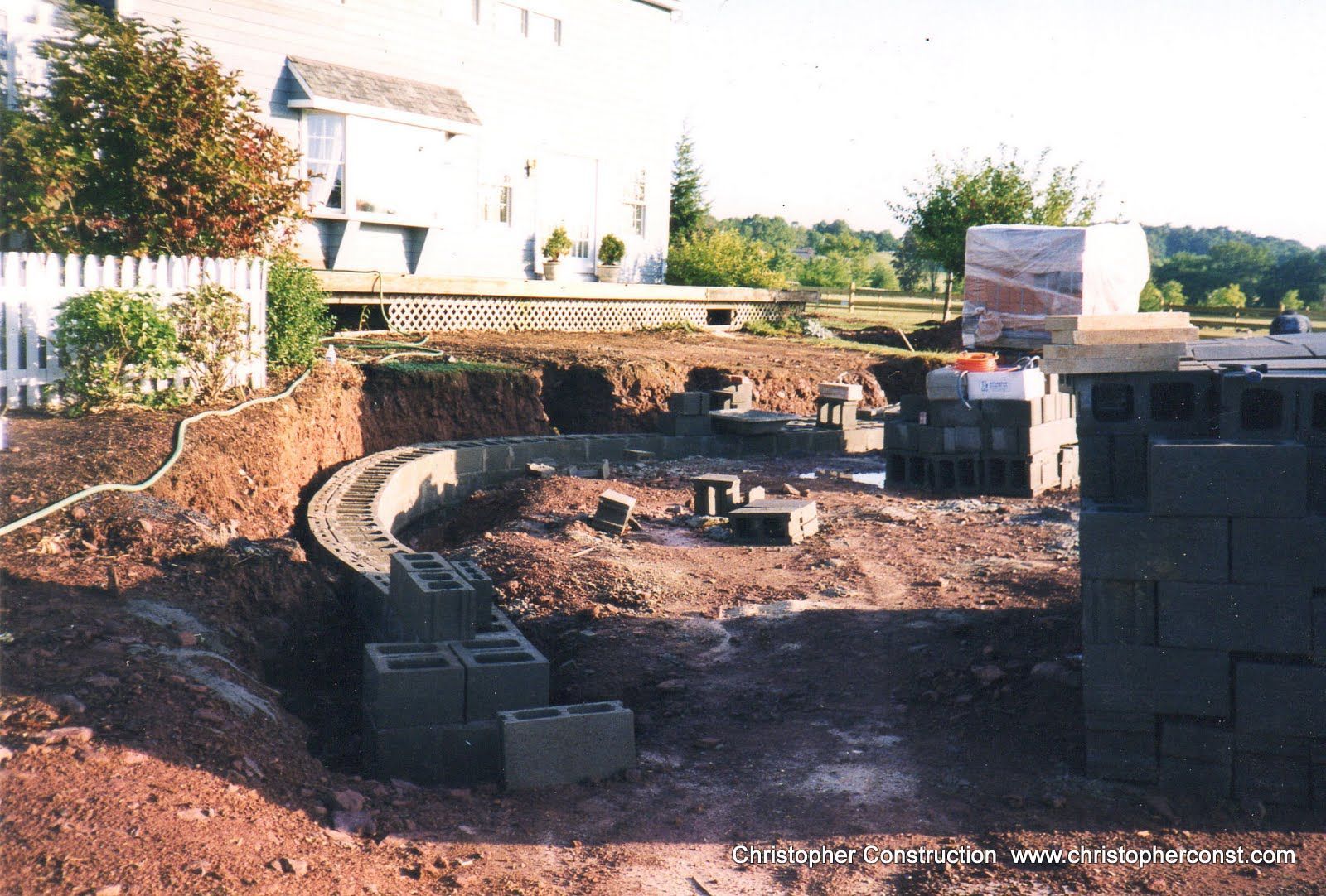 Stone retaining wall under construction in a backyard with stacked blocks and excavation trench
