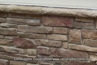 Stone veneer wall with tan and red stones beneath a light trim edge