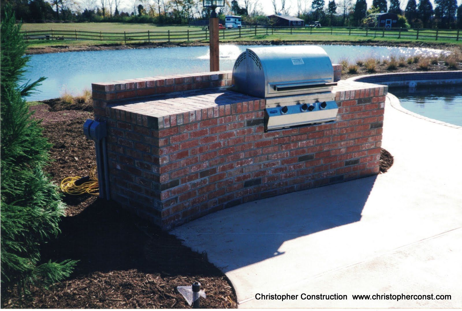 Brick outdoor grill on a curved brick wall beside a paved patio and grassy field.
