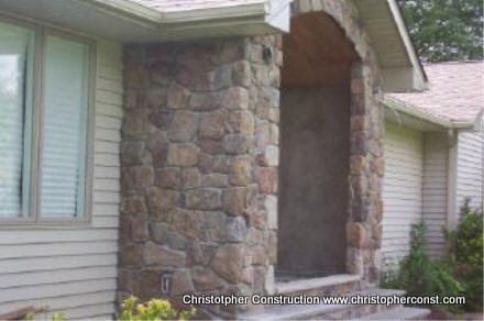Stone front porch with arched entryway and beige house siding