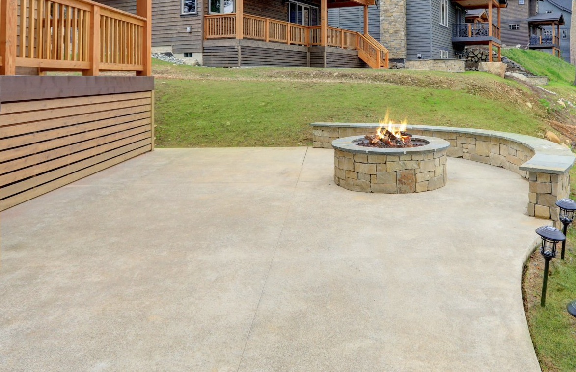 Stone fire pit on a concrete patio beside a grassy lawn and wooden deck at a residential complex