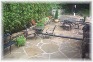 Patio with stone paving, outdoor tables and chairs, and lush green hedges along the left side