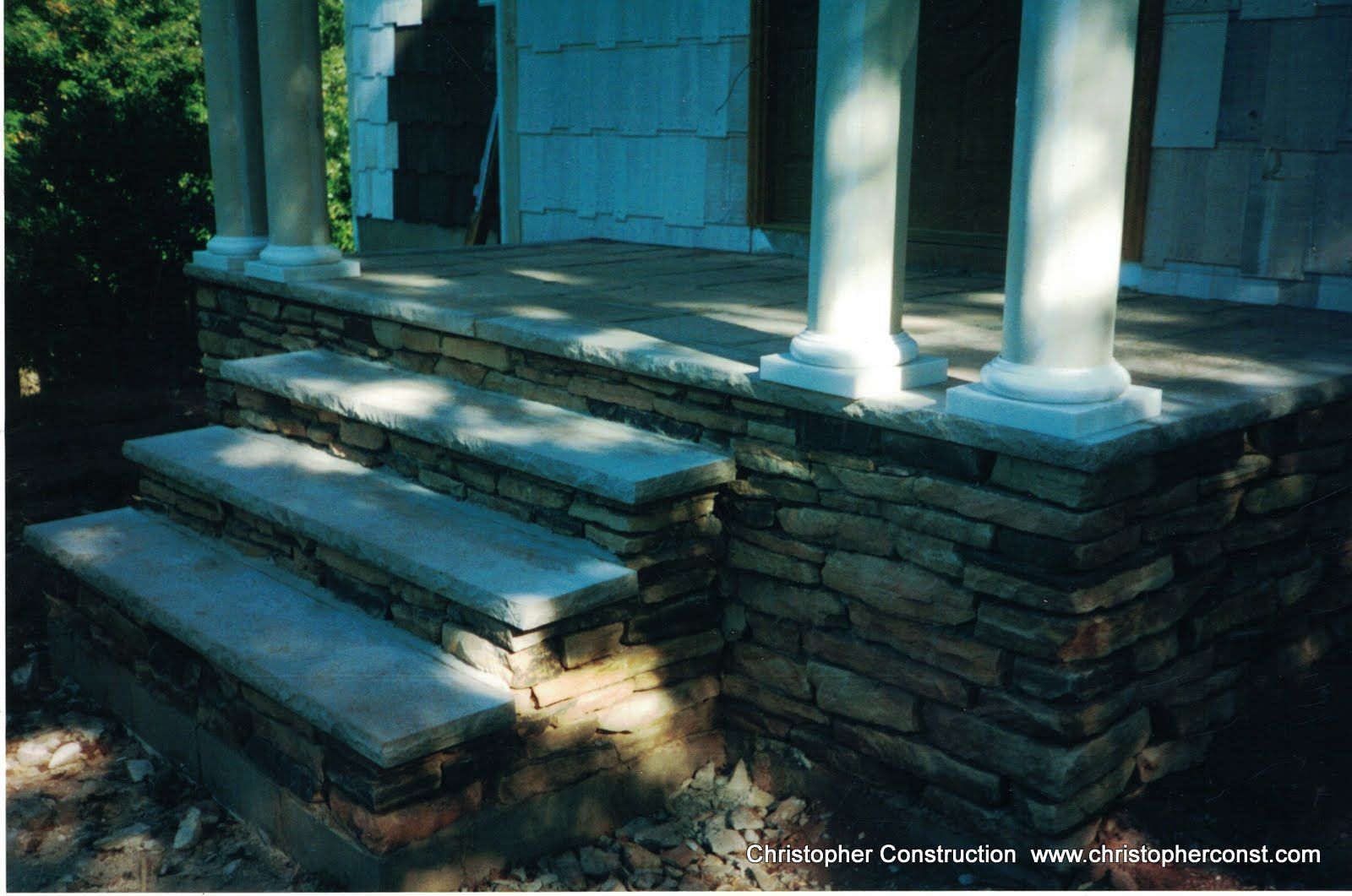 Stone steps leading to a porch with white columns in dappled sunlight