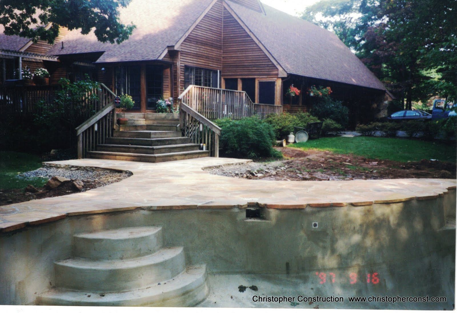 Wooden cabin with front porch and stone steps beside an empty curved swimming pool and deck