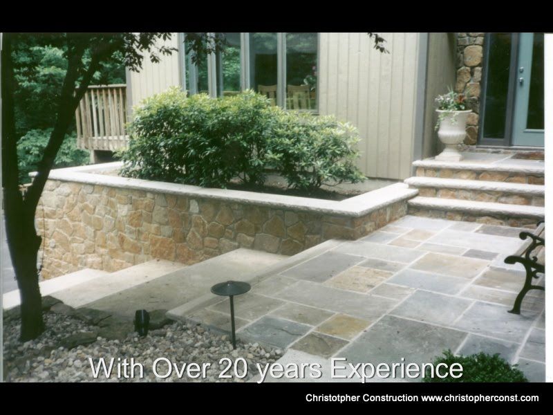 Patio with stone pavers, raised planter, steps to a house entrance, and a small tree at left