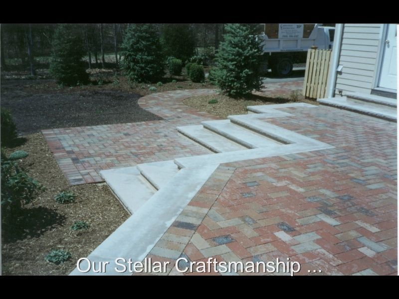 White concrete steps and paver walkway leading to a house patio beside a wooden fence and shrubs