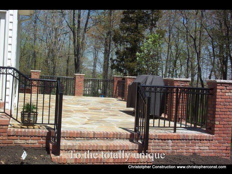 Brick patio with black metal railing and gate, bordered by red brick columns and trees in the background