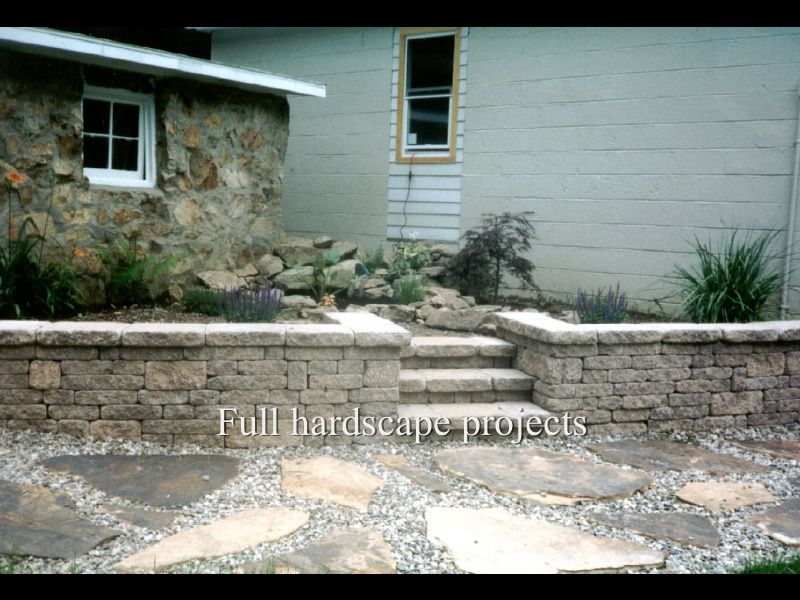 Stone patio and retaining wall in a landscaped yard beside a house