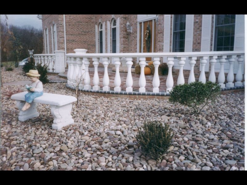 Garden bench beside a white balustrade in a rock-covered yard with a small child statue and stone house facade