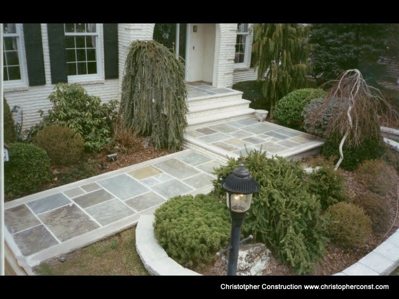 Front walkway with stone pavers, curved edging, and landscaped shrubs leading to a house entrance