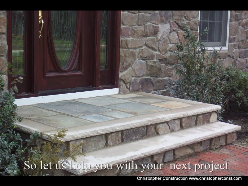 Stone front steps and landing beside a dark wood door on a stone house entrance