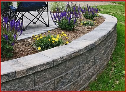 Curved stone garden wall with purple and yellow flowers beside a patio chair on grass