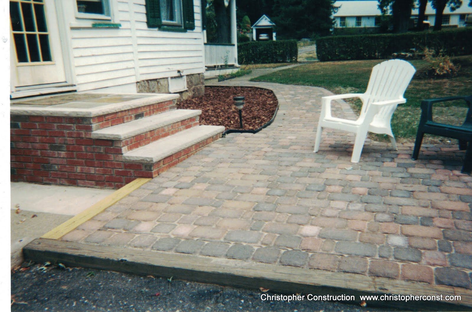 Brick patio with steps beside a house, featuring white and black lawn chairs.