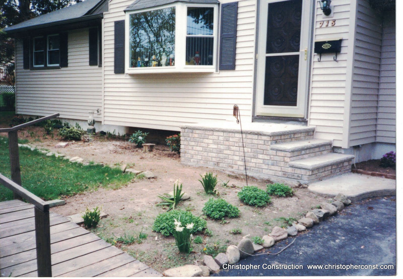 House front with small landscaped garden, stone steps, and a walkway beside the driveway