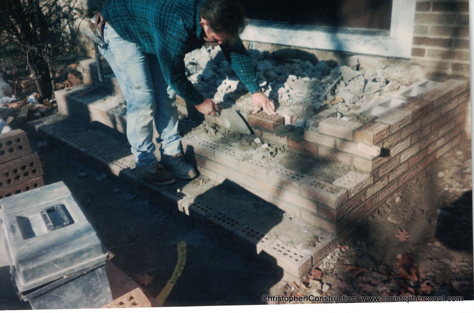 Two people stacking bricks at a construction site beside a partially built wall