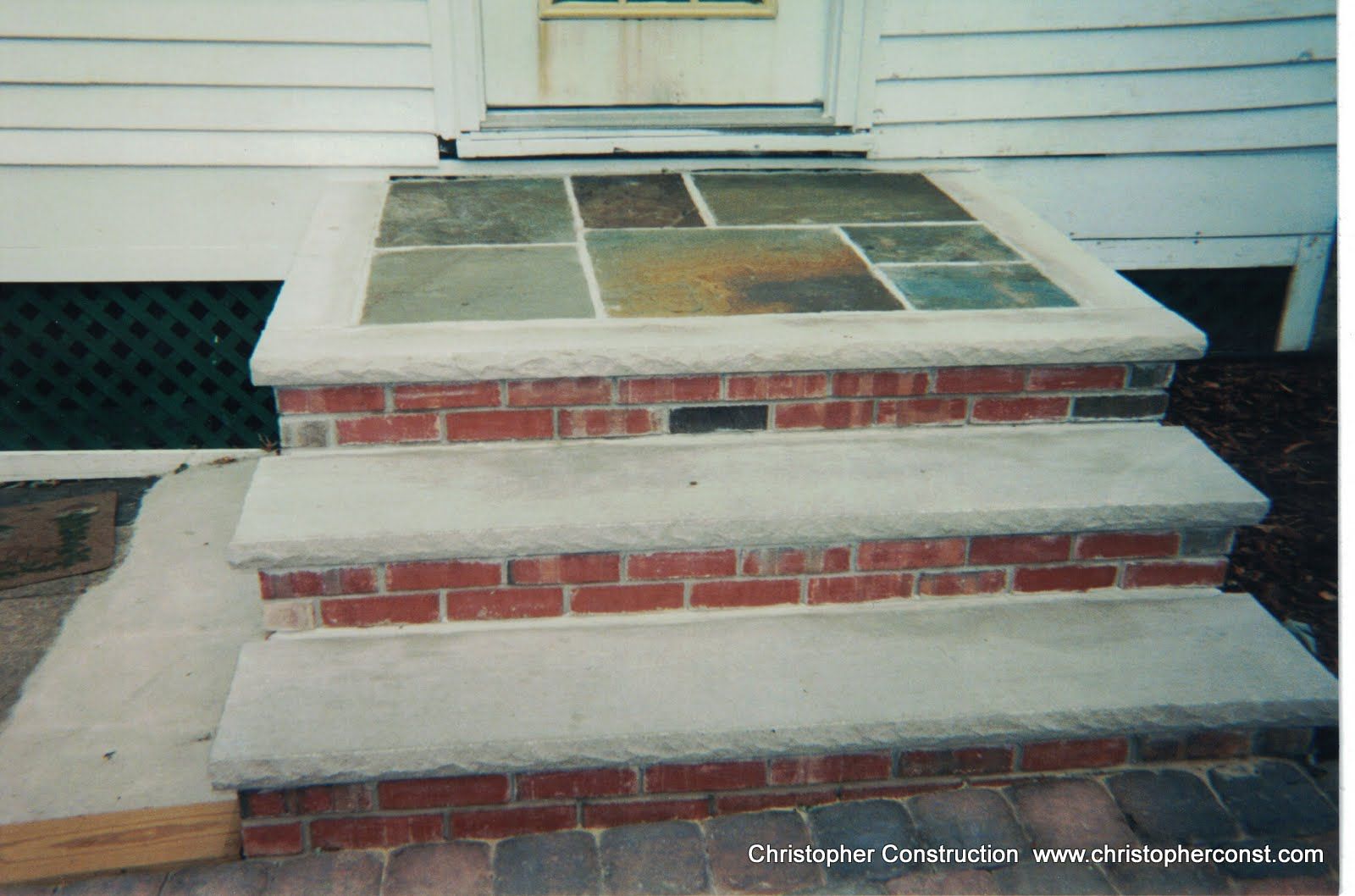 Brick front steps with wide concrete treads and tiled top landing beside a white house.