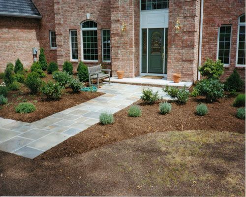 Front yard landscaping with stone walkway, shrubs, and brick house entrance