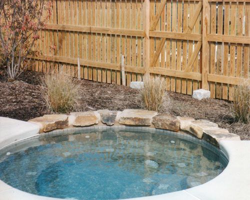 Backyard hot tub beside a wooden fence and landscaped rocks.