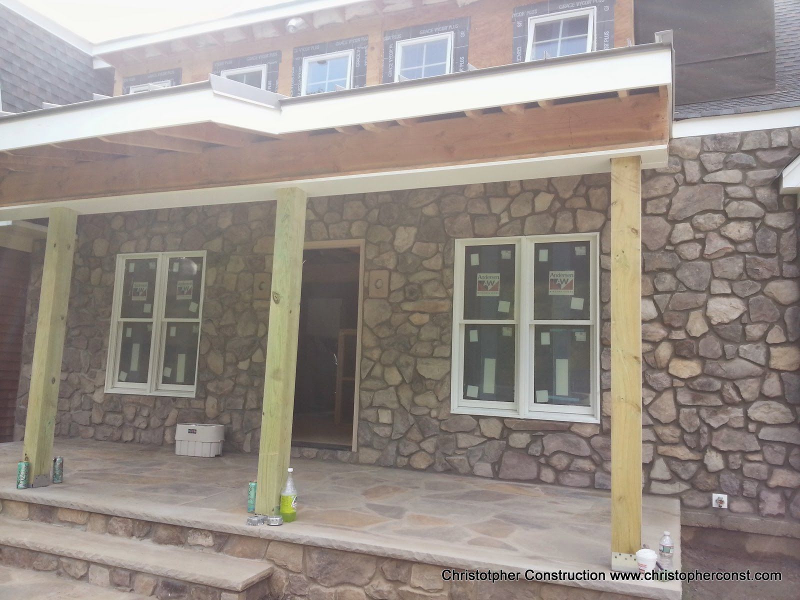 Stone-front porch with white windows and porch columns on a brick house.