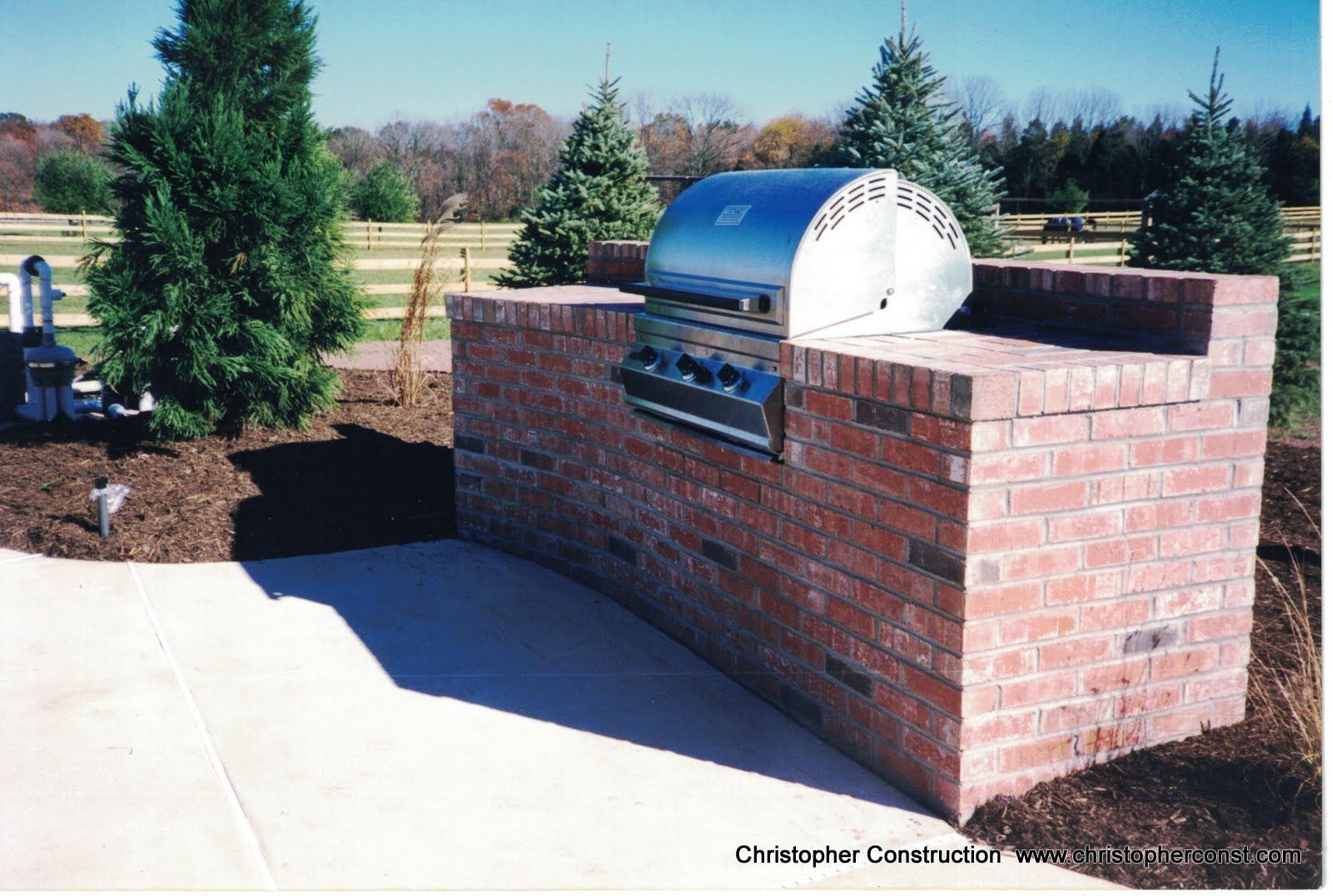Brick outdoor grill built into a brick wall in a landscaped yard