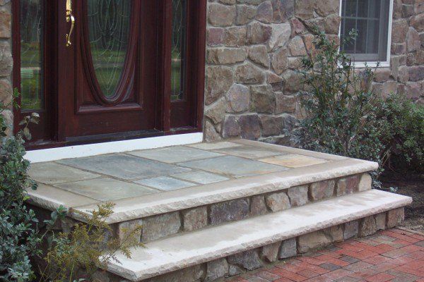 Front porch steps with a small stone landing beside a brick house and dark wooden door
