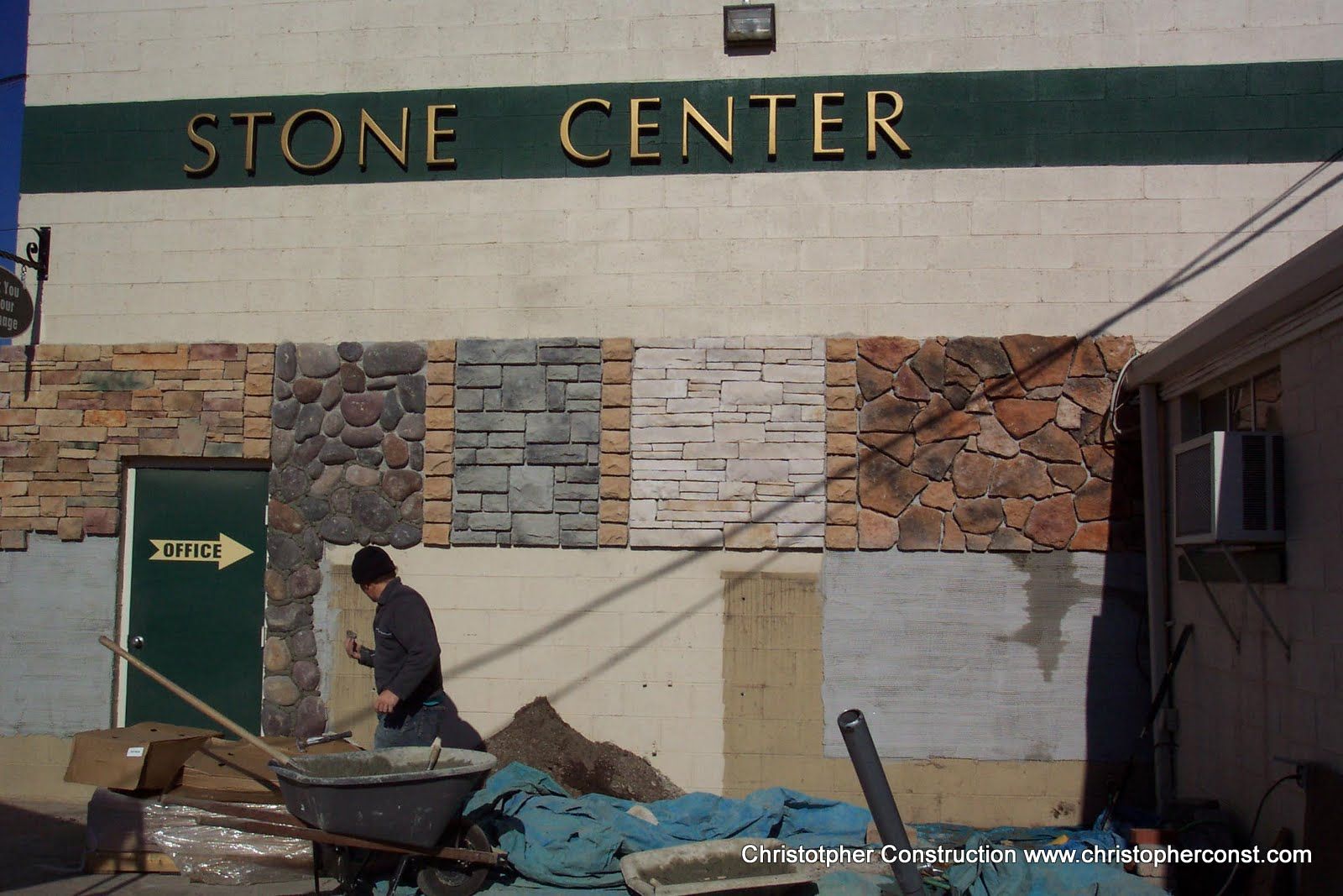Stone Center building facade with stone sample panels and a worker pushing a wheelbarrow outside