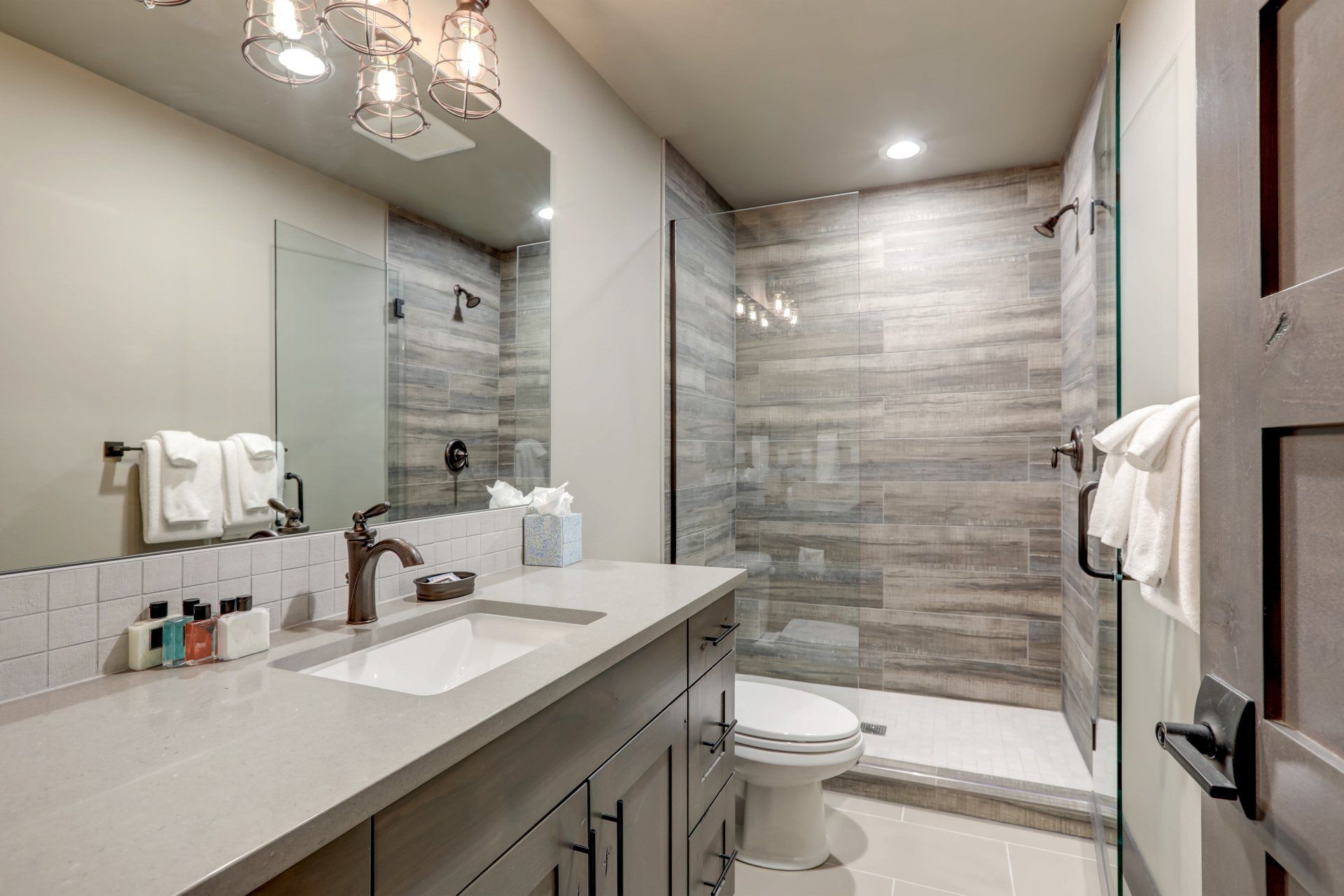 Modern bathroom with double vanity, large mirror, and glass-enclosed shower in gray tile.