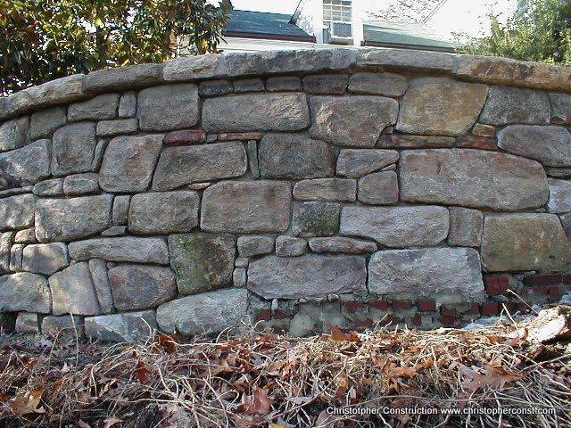 Stone retaining wall with rough gray blocks and fallen leaves at the base