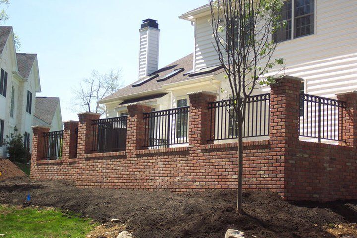 Brick privacy fence around a suburban house with black metal railings and a young tree in front