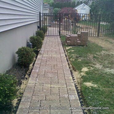 Narrow brick walkway along a house leading to a black metal gate in a backyard