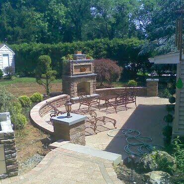 Outdoor patio with brick grill, curved bench seating, and tables in a landscaped backyard