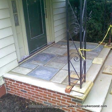 Front porch with brick steps, tiled landing, and metal railing beside a green door