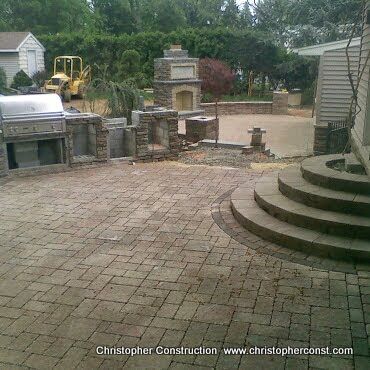 Backyard patio with stone pavers, curved steps, outdoor kitchen, and brick fireplace