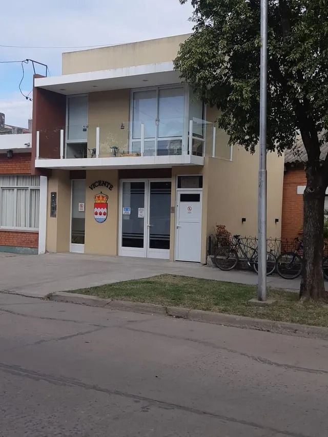 Casa moderna de dos plantas, con balcón, fachada blanca y un árbol delante, en una calle tranquila.