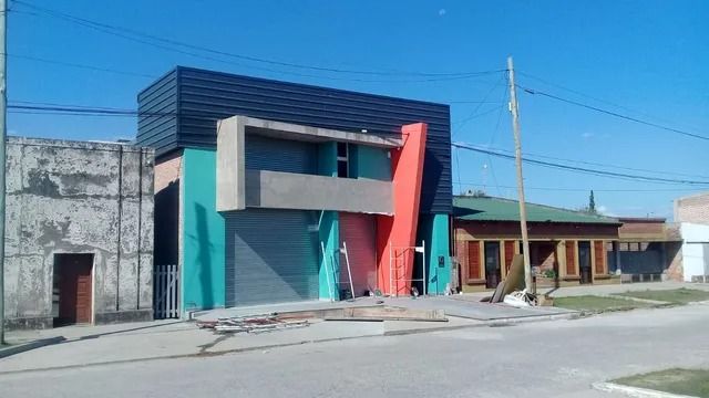 Edificio moderno y colorido en una esquina, con paneles turquesa, coral y grises bajo un cielo azul