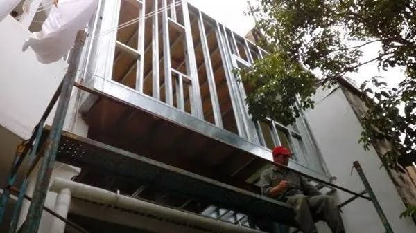 Trabajadores sobre andamios instalan vigas metálicas verticales en el exterior de un edificio.